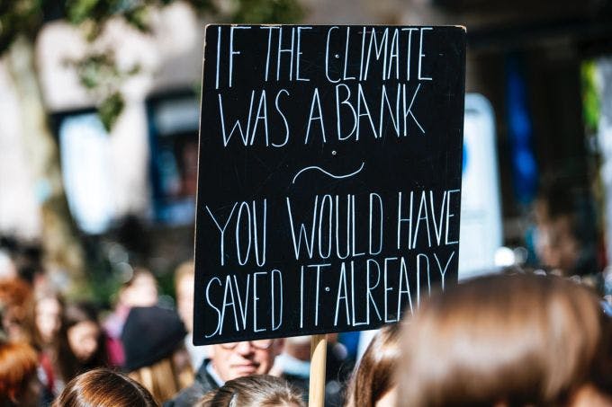Someone holding up a sign that reads, "If climate was a bank, you would have saved it already."